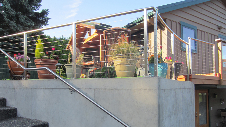 Wire rail with round handrail on patio. Stainless steel round handrail on stairs. The handrail is attached to a concrete wall.