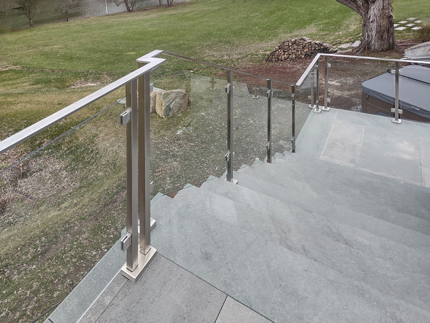 Glass patio railing system with a surface mount post on stone looks very modern.