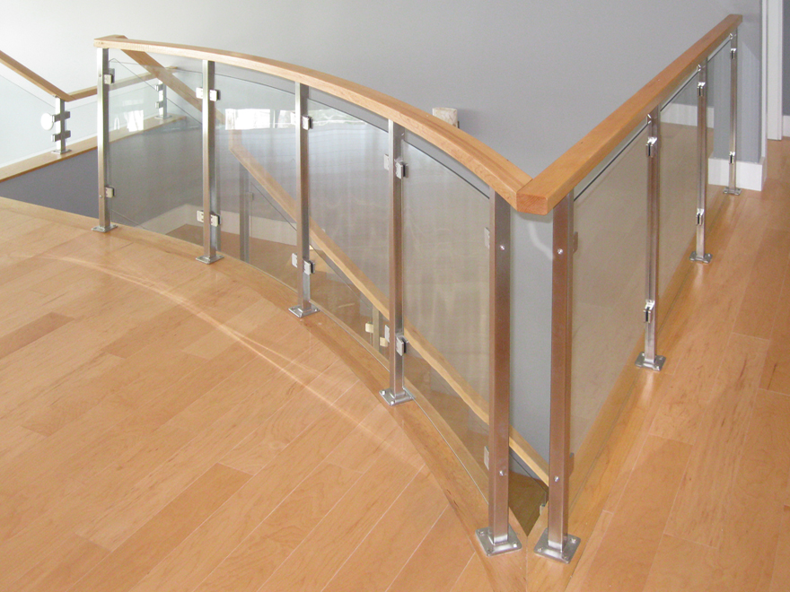 Curved wood and glass staircase railing on landing. Glass railing posts are custom-designed.