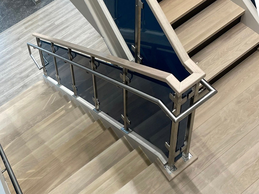 An AGS glass handrail is simple to install. This blue glass handrail has a wood cap rail and stainless grabrail. Handrail brackets are attached to the railing posts to secure the latter in place.